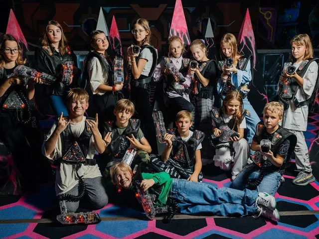 Команда подростков в игровых жилетах с бластерами на лазертаг-арене LaserLand