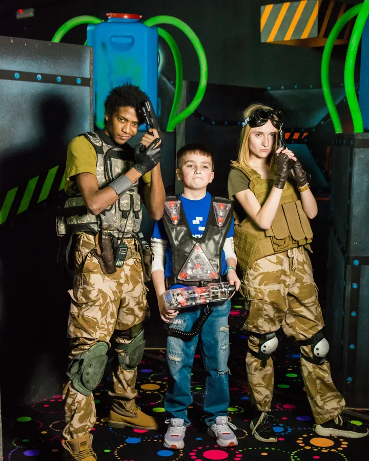 Ведущие праздника в экипировке и именинник с бластером на арене LaserLand